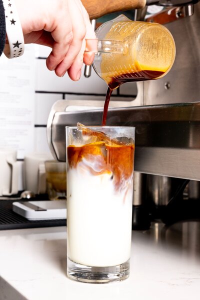 Barista pouring espresso over milk to create an iced latte at Grain Artisan Bakery & Craft Coffee in Snohomish, WA.