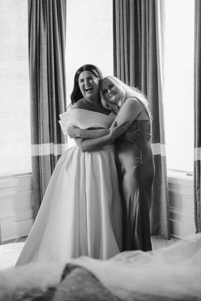bride hugging bridesmaid in window at the madrona during wedding getting ready