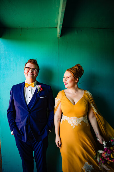 A wedding couple at the Toledo Zoo standing side by side in front of a teal wall