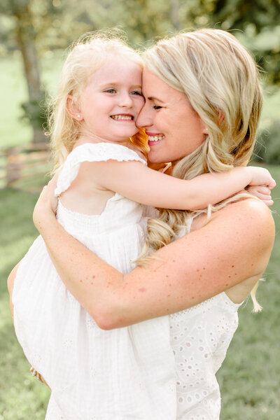 Mom hugs young daughter in a field during a family session at Cherokee Bluffs Park in Flowery Branch