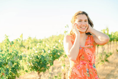 High school senior girl in an orange dress standing in front of a vineyard
