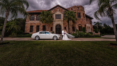 Bride and groom standing next to a luxury car in front of The Howey Mansion