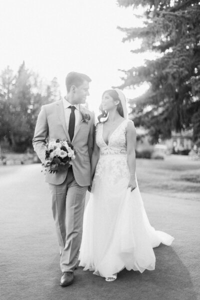 a black and white photography of a bride and groom walking acroos a lawn during their Alberta summer wedding photographed by Calgary wedding photographers David and Breanne Heidrichotography studio