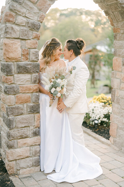 Bride and bride embracing under a stone archway during their outdoor wedding, captured by Nashville wedding photographer Diana Marie.