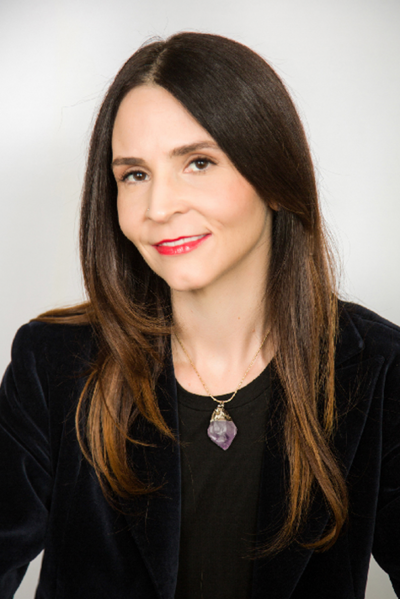 Headshot of a woman with long brown hair wearing a blue blazer and blue and white polka dot blouse