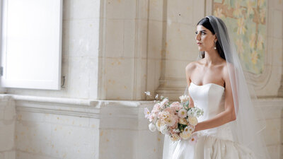 Kaitlyn holding a bouquet inside a Loire Valley French chateau, exuding elegance and joy on her wedding day.