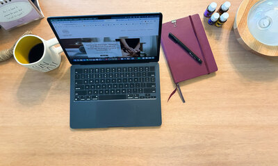 Flat lay of laptop displaying LivingTree Wellness site with coffee, diffuser, journal, and essential oils