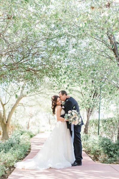 Groom kissing bride on cheek surrounded by trees at El Chorro  Wedding Venue