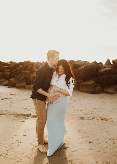 Expecting couple holding baby bump during a beach maternity session in Orange County, California 