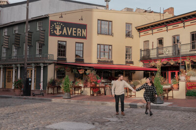 couple walking across city cobblestone street holding hands