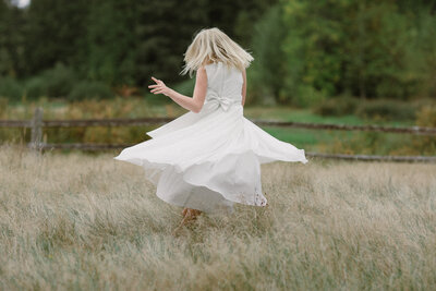 Floer girl twirling in a grassy field at a Seattle wedding.