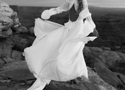 woman with wedding dress blowing in the wind standing in front of canyon