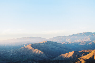 Dramatic sunset view of the Santa Ynez Mountains in Santa Barbara, California. Golden hour landscape photography showcasing the rugged coastal mountain range with soft pastel sky. Architectural peaks and valleys cast in dramatic light and shadow. Perfect backdrop for luxury Santa Barbara weddings and elopements.