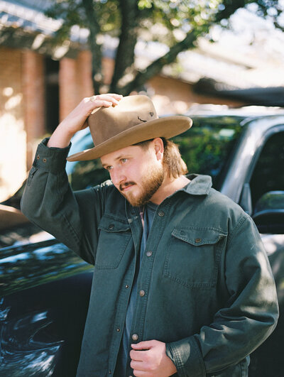 Man in a button down jacket adjusting a western style hat on his head