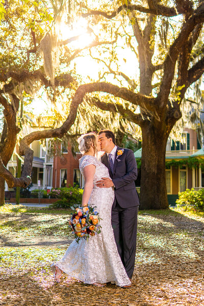 Bride & Groom kissing with large bouquet at Forsyth Park wedding venue in Savannah, GA. Weddings in Savannah, GA.