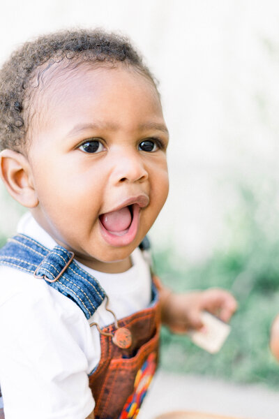 African American boy with brown hair and brown eyes wearing white shirt and denim overalls taken by New Orleans wedding photographer Elizabeth Collins