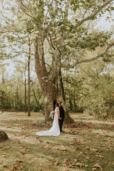 Couple standing together beneath a large tree in an autumnal setting