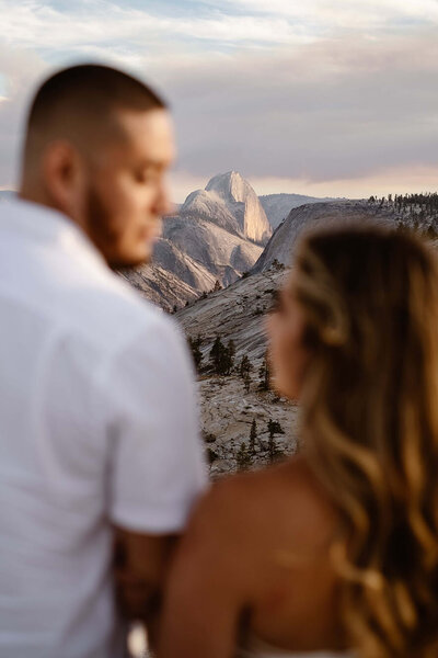 Couple looking at one another as they are out of focus with Half Dome in focus in the middle.