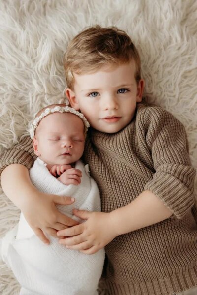 Family portraits of a little boy holding his nerborn baby sister in michelle kelly's photography studio