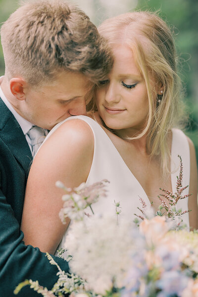 Groom kissing bride on the shoulder from behind.