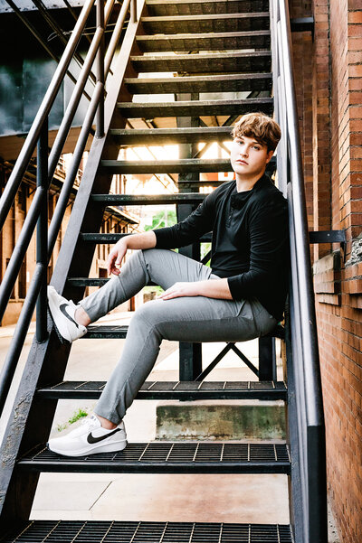 High school senior boy sits on a metal staircase outdoors at the High Line in downtown Pittsburgh.