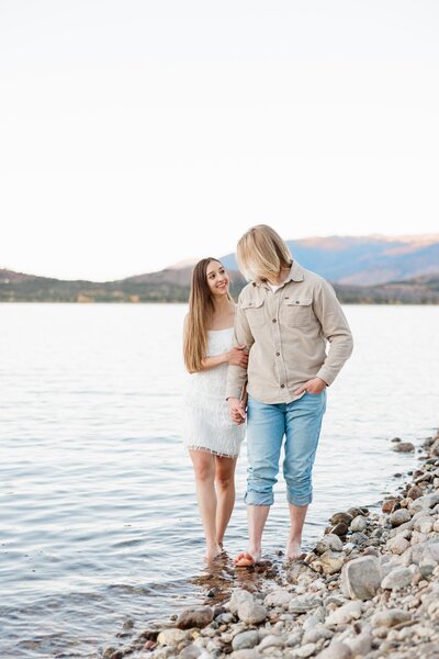A couple smiles while walking in a shallow alpine lake as guided by their Breckenridge Couples Photographer
