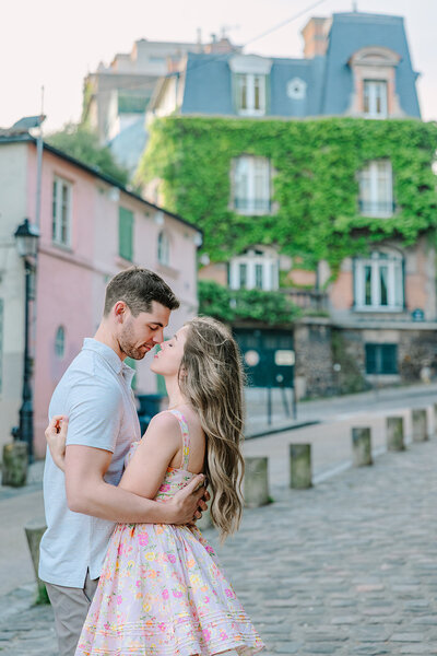 Man and woman holding each other close and leaning in for a kiss during a romantic Paris couples photoshoot near Sacré-Cœur and rue de l’Abreuvoir in Montmartre.