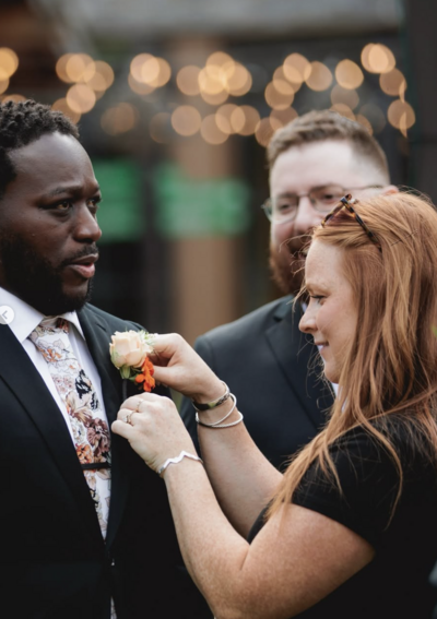 Katie Hopkins, owner, event planner, and designer, putting a corsage on a groom and wedding client on the day of his wedding.