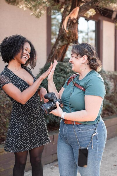 two women giving each other a high five while one holds a camera