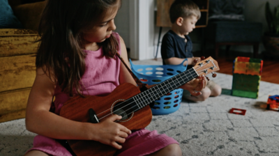 young girl plays her ukulele while her brother builds with blocks