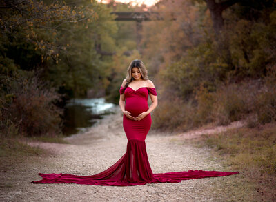 pregnant woman wearing red fitted dress next to a creek