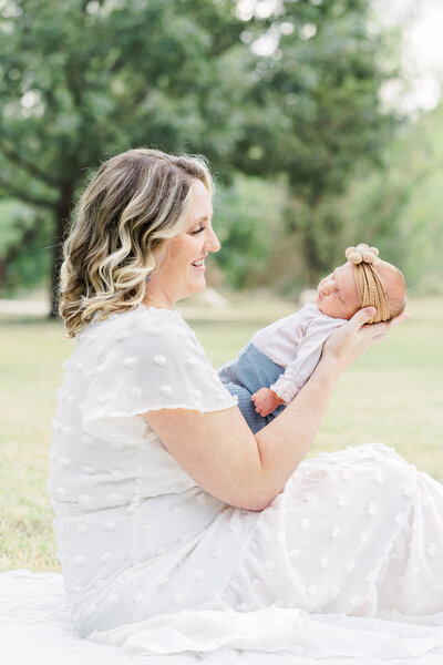 A pregnant woman dressed in a pale pink dress stands in a field of tall grass at Brushy Creek Lake Park. She looks down at her belly with a soft smile of her face in this tender shot captured by a Cedar Park Maternity Photographer