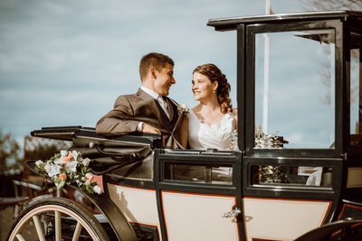 as strahlende Brautpaar geniesst eine romantische Fahrt in einer Hochzeitskutsche von Kutschenfahrten Scherrer und teilt lachend ihre Freude.
