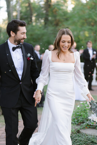 Newlyweds joyfully walk hand-in-hand through a garden celebration