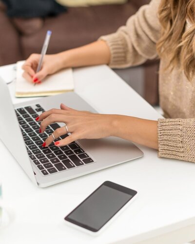 WOMAN TYPING ON LAPTOP AND PEN ON NOTEPAD