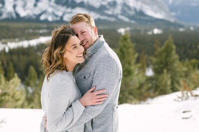This heartwarming image captures a fiancé hugging his partner from behind during a winter photo shoot on Lake Louise. The snowy landscape and icy backdrop enhance the warmth and closeness of their embrace, encapsulating a perfect moment of love and connection in the chilly setting.