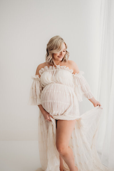 pregnant woman holding dress in denver maternity studio with photographer