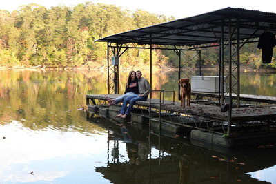 woman and man sitting on bank of river with dog