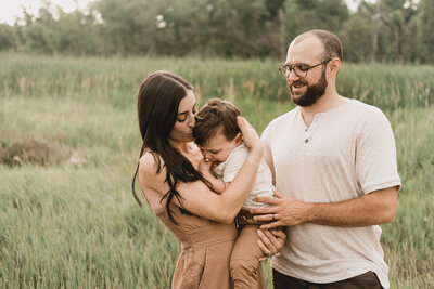A couple embraces their little one while wondering through a field during an extended family photoshoot near bismarck, ND