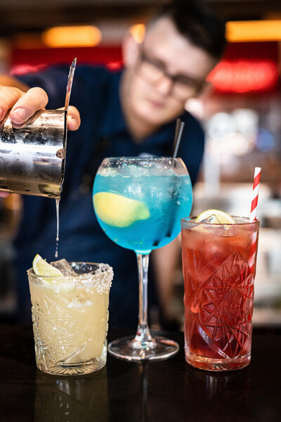 Corporate branding photography on the Central Coast showing a bar tender pouring colourful cocktails. The drinks are close to the camera, whilst the bar tender is blurred in the background.
