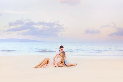woman leans back on her boyfriend at the beach surrounded by a beautiful pastel sky