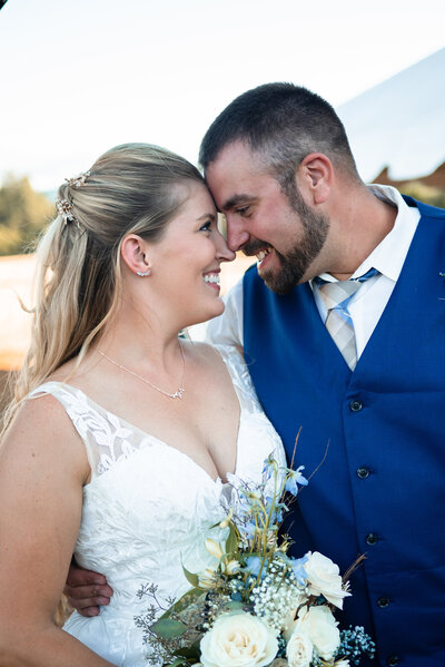 Heartwarming photo of a bride and groom embracing on their wedding day in Salem, Oregon. The bride, in a beautiful white gown, and the groom, in a sharp blue vest and tie, share a tender and joyful moment, showcasing the love and happiness of their special day.