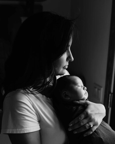 Mom holding baby while looking out the window by taylor lynn studios