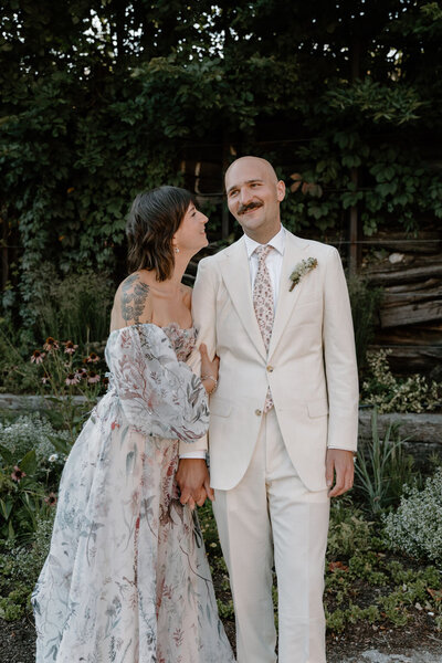 Bride in earthy, flowy, watercolor-printed dress holds groom's hand as he smiles off camera