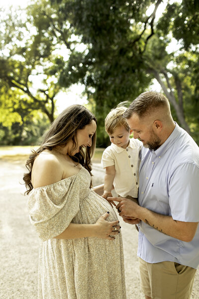 Expecting mom at parkA heartwarming maternity photo at the park, with the expecting mom standing alongside her husband and young son, as the son lovingly touches her belly, captured by Chunky Monkey Photography.