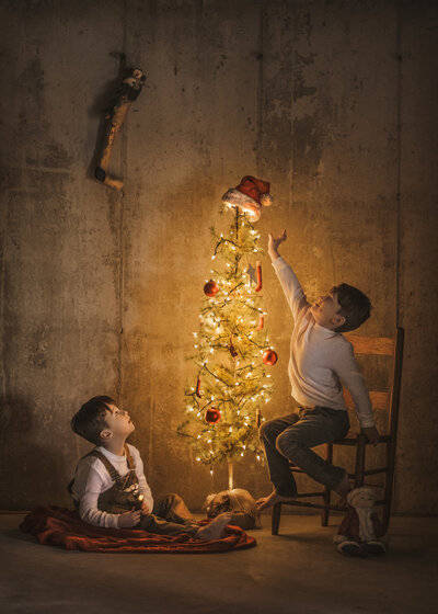 twin siblings reach for christmas tree during holiday mini sessions in hamilton, new jersey.