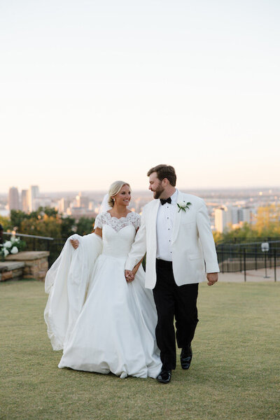 Couple walks with the city in the far distance on a grassy hill
