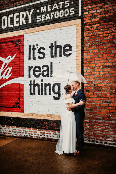 a Washington wedding couple embracing in front of vintage Coca-Cola mural in the rain - downtown