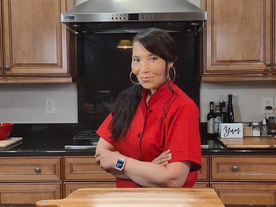 Chef Regina standing at her  kitchen counter, wearing a red blouse and hoop earrings