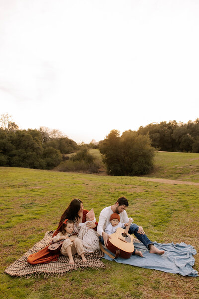 Family sitting on blankets and playing guitars together during a relaxed family session in Los Angeles